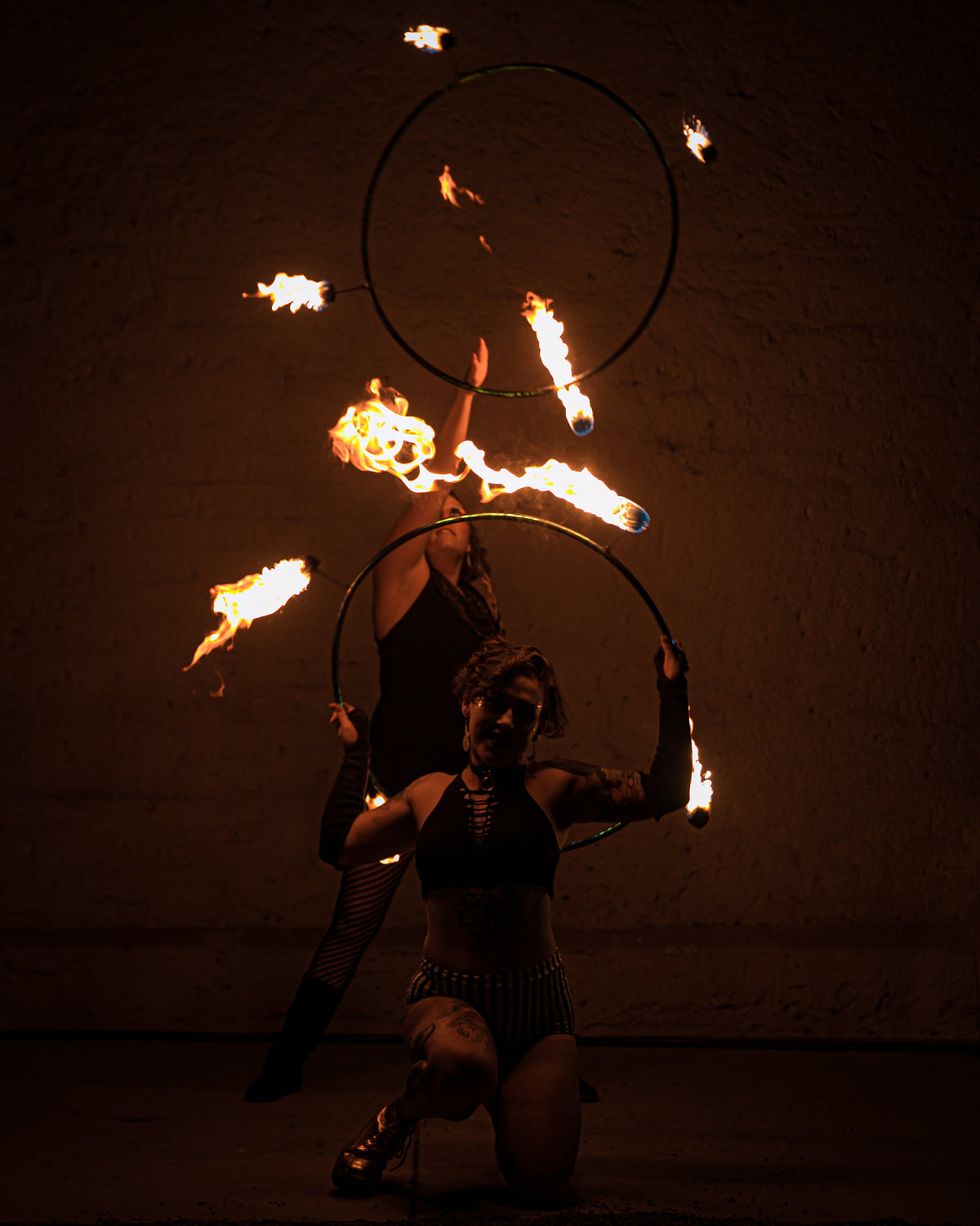 Two fire hoop rings with burning wicks, performer crouching and holding props.