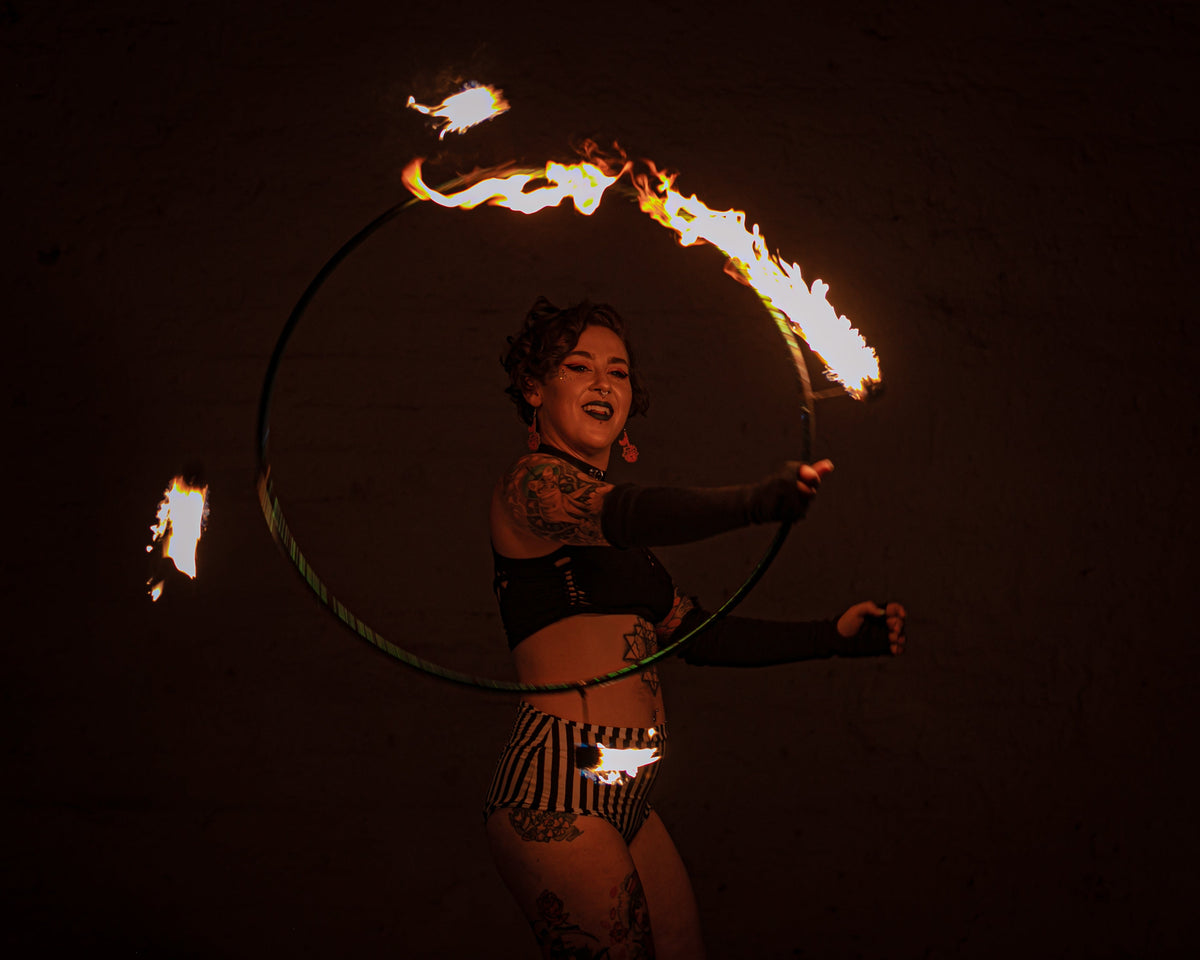 Fire hoop ring with burning wicks, performer holding prop with arms extended.