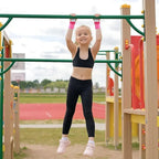 Child wearing pink aerial grip wristbands while hanging from an outdoor play bar