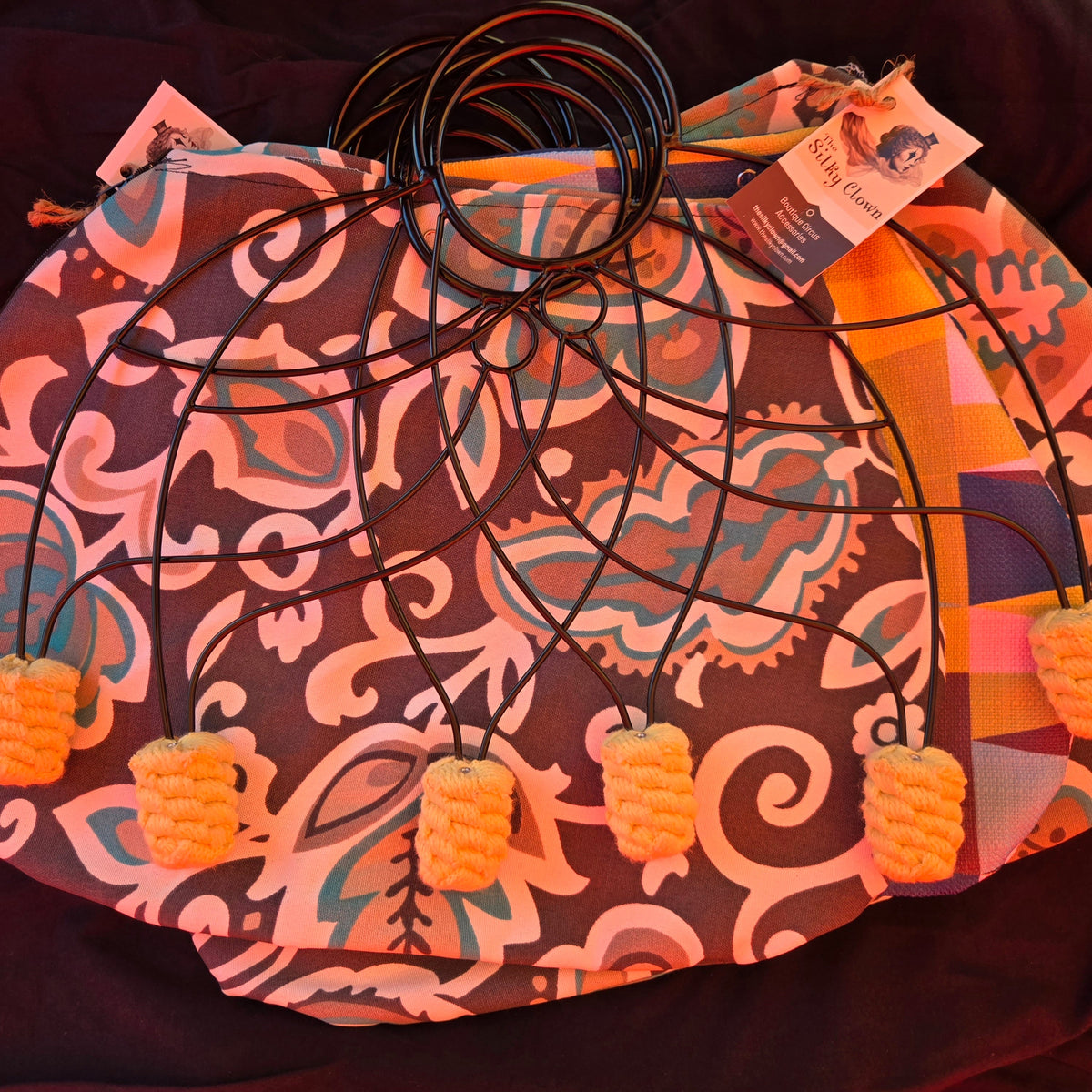 Patterned fan cover with black cord ring stays and orange pom-pom tassels at corners.