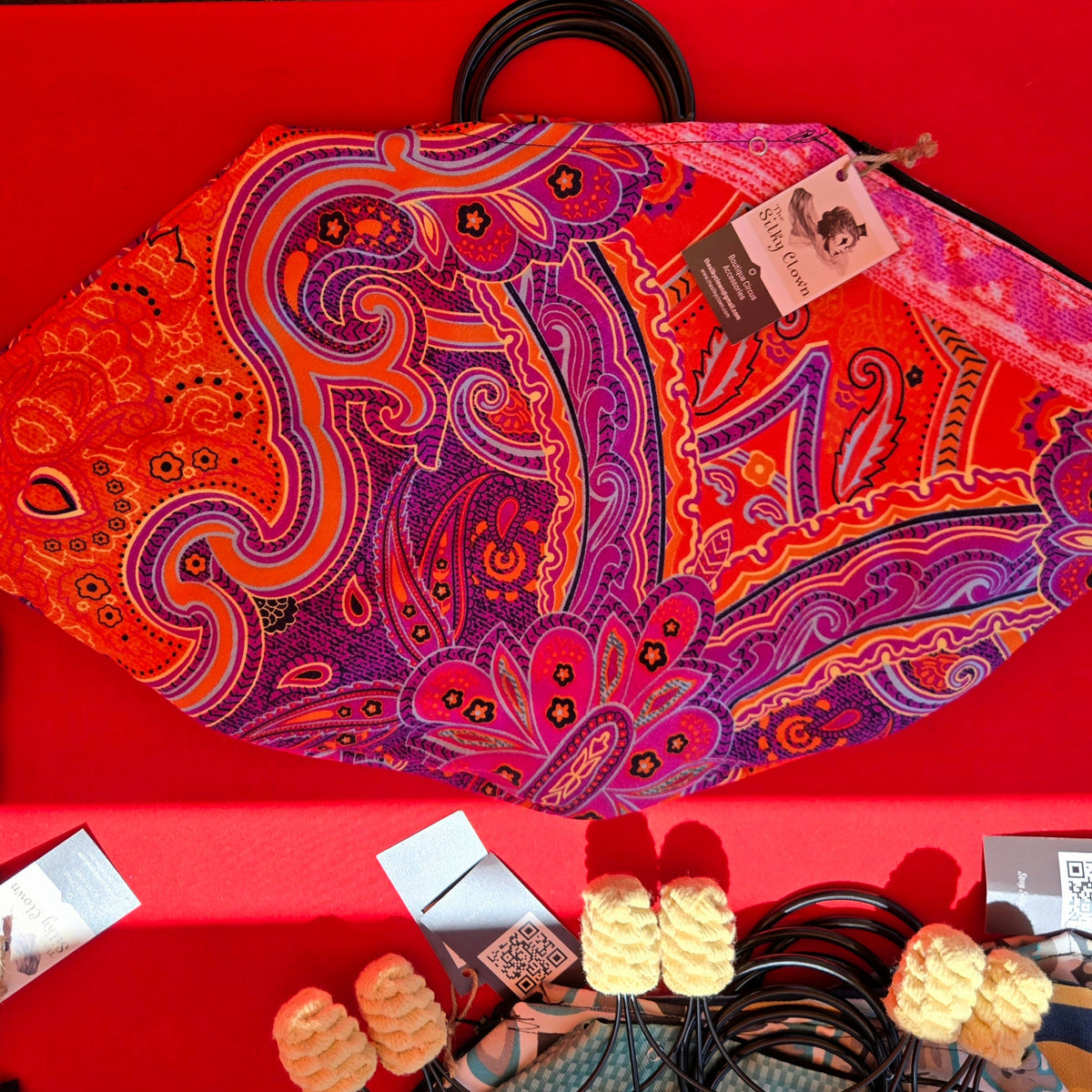 Paisley fan cover with purple and orange design, black cord ring stays, and pom tassels.